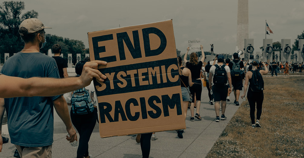 A cardboard sign that says "end systemic racism."