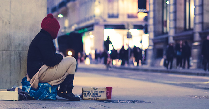 A person, who is presumed homeless, sits on the corner of a street.