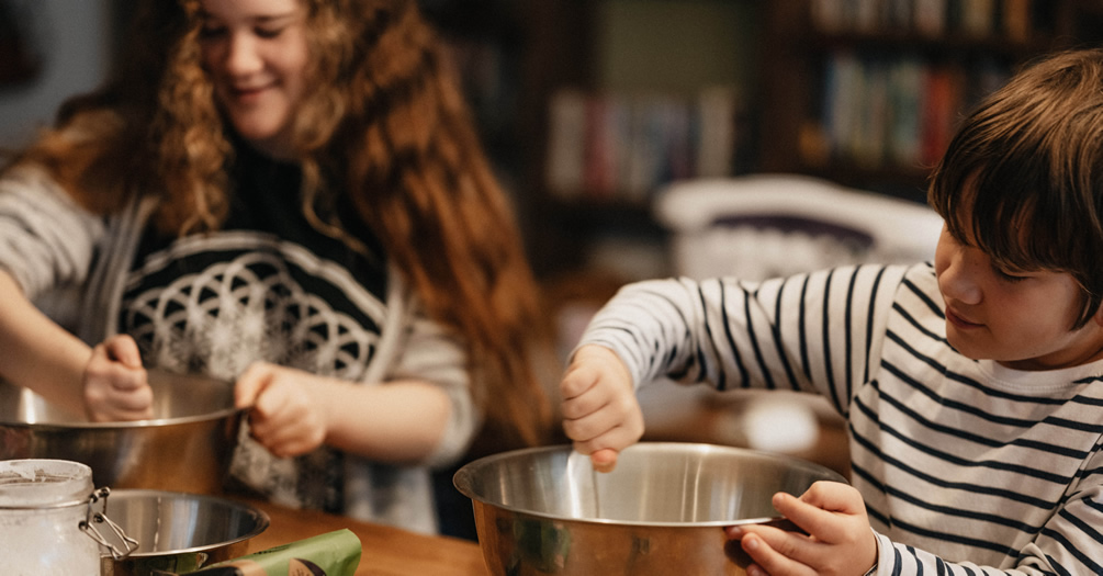 Two children stirring in metal bowls in a kitchen.