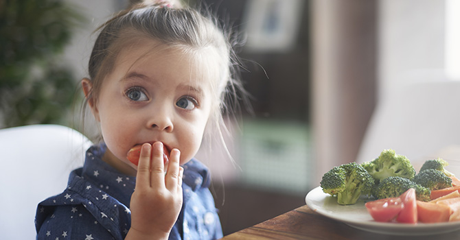 Young child eating vegetables at a table. 